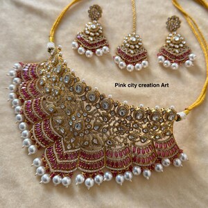 May include: Gold-toned necklace and earring set with ruby-colored accents and white pearls. The necklace features intricate filigree and sparkling clear stones. The set includes matching earrings and a headpiece. Text on the image reads "Pink city creation Art."