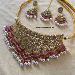 May include: A gold-toned necklace and earring set with a matching headpiece. The jewelry features intricate filigree designs, clear gemstones, and pink accents. The necklace and earrings are adorned with white pearls. The text "Pink city creation Art" is visible.