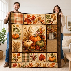 Pode incluir: Uma colcha retangular com um design de patchwork de painéis com tema de outono. As imagens incluem abóboras laranja, talos de trigo, bolotas, folhas de bordo vermelhas e douradas, bagas e um jarro de metal, tudo emoldurado por uma borda marrom escura.