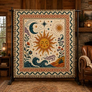 May include: A woven throw blanket featuring a central sun face with closed eyes, surrounded by a crescent moon, stars, swirling waves, and floral motifs. The design includes a decorative border with wavy lines and geometric patterns in cream, gold, blue, and rust tones.