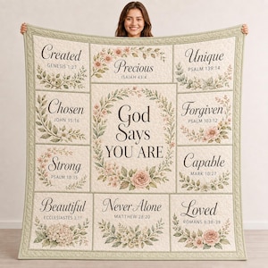 Op de afbeelding: Een crèmekleurige quilt met een centrale bloemenkrans met de tekst God Says YOU ARE, omringd door tien rechthoekige panelen. Elk paneel bevat een woord zoals Created, Precious, Unique, Chosen, Forgiven, Strong, Capable, Beautiful, Never Alone en Loved, gecombineerd met bijbelverzen en botanische illustraties.