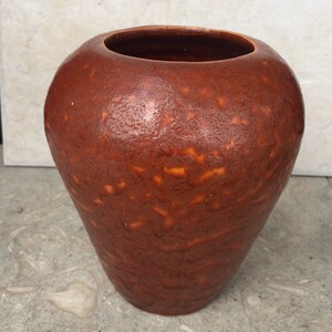 May include: A brown ceramic vase with a textured surface. The vase has a rounded body and a narrow opening.