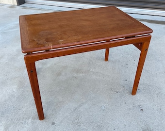 May include: A rectangular, mid-century modern wooden table with a dark brown finish. The table has a simple design with four angled legs and a slightly raised edge around the tabletop. The table measures approximately 30 inches long and 18 inches wide.