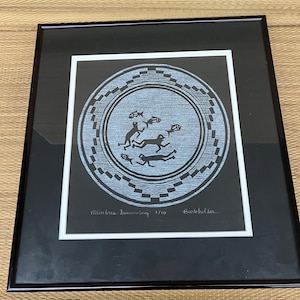 May include: Framed artwork featuring a circular design with stylized figures swimming around fish. The artwork is in a black frame with a white mat. The text "Mimbres Swimming 1/10 Burkholder" is visible.