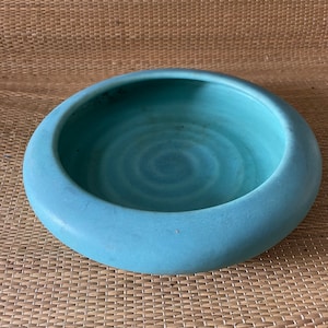 May include: A light blue ceramic bowl with a rounded shape and a slightly textured surface. The bowl has a subtle swirl pattern in the glaze.