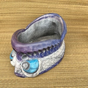 May include: A ceramic planter shaped like a fish with blue and purple glaze. The planter has a textured surface and a wide opening at the top.