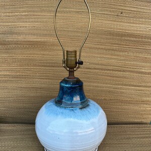 May include: A white ceramic table lamp with a blue glaze and a brass lampshade. The lamp has a round base and a tall, slender neck.