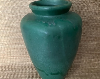 May include: A green ceramic vase with a rounded body and a wide opening. The vase has a matte finish and a slightly textured surface.