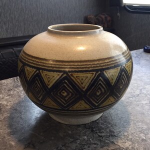May include: A round ceramic vase with a geometric pattern in shades of brown, yellow, and black. The vase has a speckled white glaze.