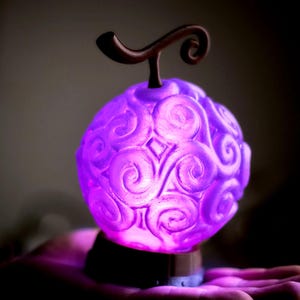 May include: A glowing purple orb with swirling patterns, topped with a brown stem. The orb is lit from within, creating a soft glow. The base is dark, and the overall effect is fantastical. A decorative item.