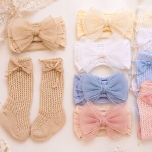 Könnte beinhalten: Eine Kollektion aus weichen Strickstirnbändern und passenden kniehohen Socken in Pastellfarben wie Beige, Weiß, Blau und Rosa. Jedes Stirnband hat eine große, mehrlagige Tüllschleife. Die Socken weisen eine Zopfstrickstruktur auf.