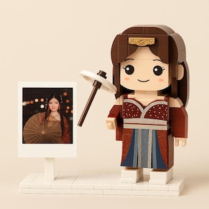 May include: A brick-built figure of a woman in a traditional Asian-inspired outfit, holding a parasol. The figure has a brown hair and a red and blue dress. A photo of a woman with a parasol is next to the figure.