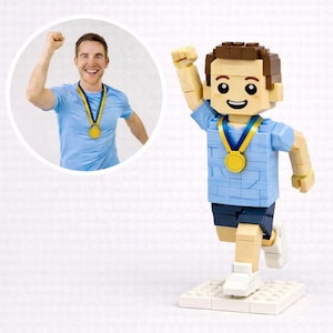 May include: A Lego-style figure of a person in a blue shirt and dark blue shorts, with a gold medal around their neck, celebrating a victory. A circular image of a person wearing the same outfit is in the background.
