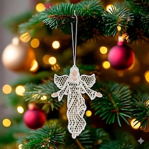 May include: A white embroidered angel Christmas ornament with open wings and a flowing gown, hanging from a green Christmas tree. The ornament has intricate details and is suspended by a thin white string. Red and gold baubles are visible in the background.