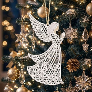 May include: A white, intricately designed angel Christmas ornament with detailed wings and a flowing gown. The ornament is suspended from a gold string and hangs on a decorated Christmas tree with other ornaments and lights.
