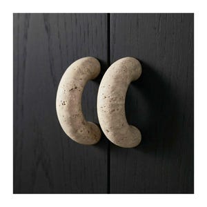 May include: Two beige, curved cabinet handles with a textured surface are mounted on a dark wood cabinet. The handles are in a crescent shape, adding a unique design element to the furniture.