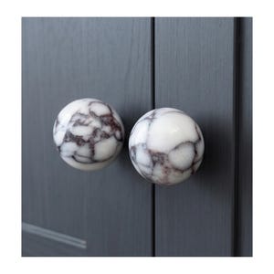 May include: Two marble cabinet knobs with a white base and gray veining. The knobs are round and mounted on a gray cabinet door. These decorative knobs add a touch of elegance to any furniture piece.