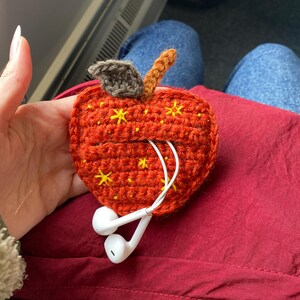 Crochet pouch for wired earphones. Small red apple with yellow embroidered stars, brown stem and dark green leaf on top