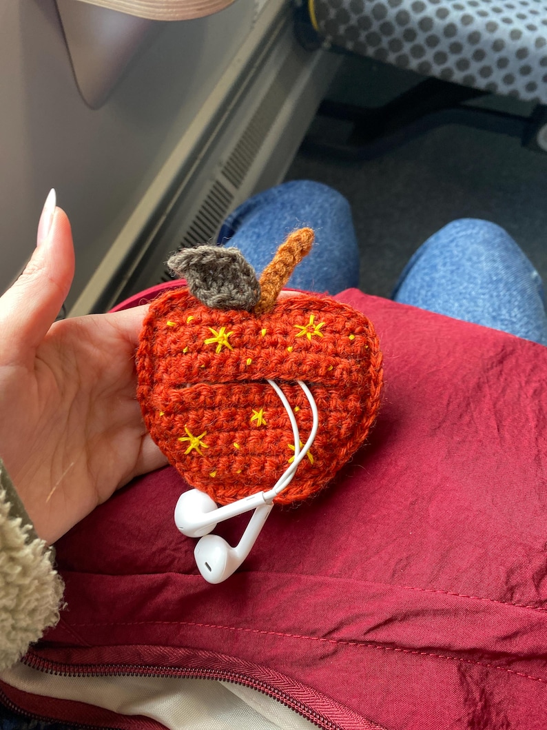 Crochet pouch for wired earphones. Small red apple with yellow embroidered stars, brown stem and dark green leaf on top