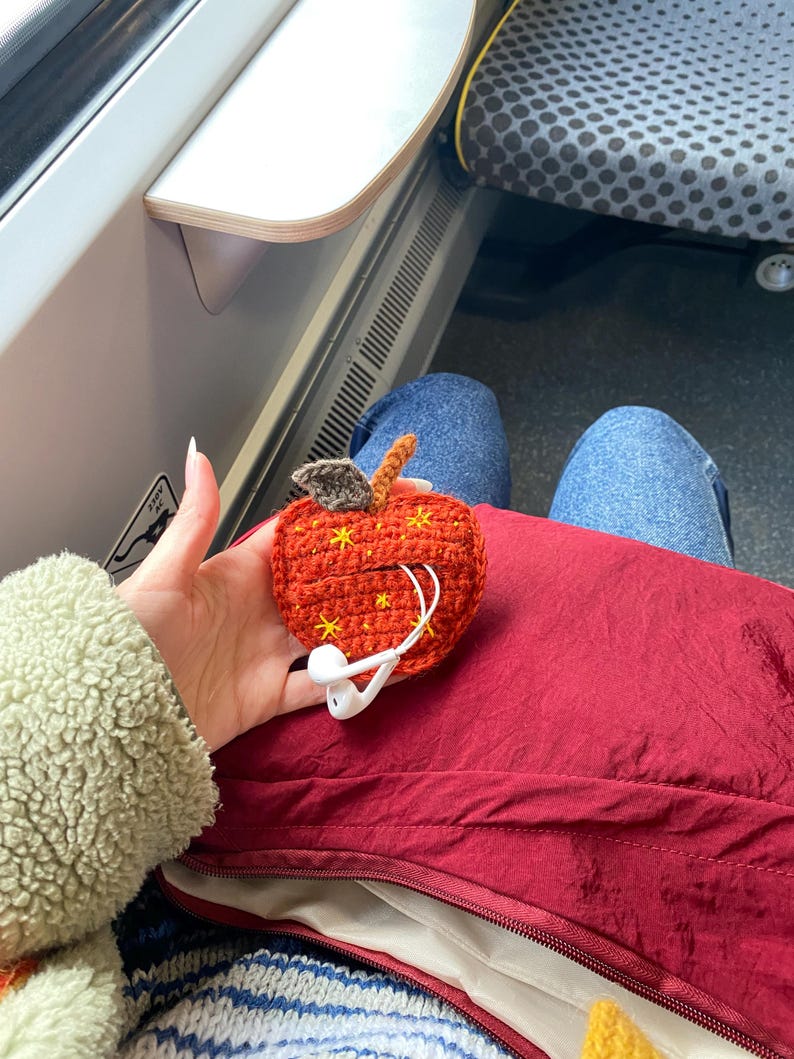 Crochet pouch for wired earphones. Small red apple with yellow embroidered stars, brown stem and dark green leaf on top