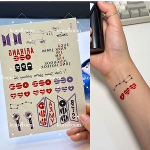 Könnte beinhalten: Ein Bogen temporärer Tattoos mit verschiedenen Designs, darunter Herzen, Sternbilder und die Buchstaben "BTS" und "ARMY". Das Blatt enthält auch Text in Koreanisch und Englisch. Auf dem Handgelenk einer Person sind Sternbild- und Herz-Tattoos zu sehen.