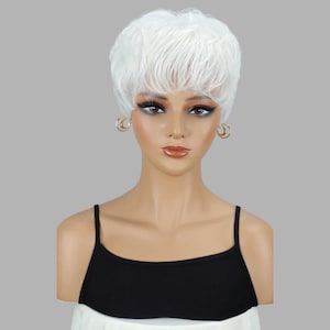May include: A white, short-layered wig styled on a mannequin head. The wig features a textured, voluminous design. The mannequin is wearing a black camisole and gold hoop earrings. The background is a solid gray.