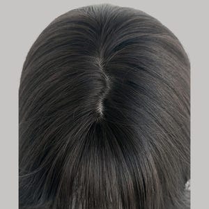 May include: Close-up of a dark brown wig with a visible part. The hair is styled with a natural look, and the strands appear smooth and straight. The wig is likely designed for fashion or cosmetic purposes.
