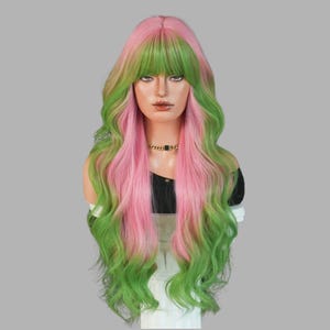 May include: A long, wavy wig with a two-tone color scheme of pink and green. The wig features a fringe and is styled on a mannequin head. The pink color is concentrated at the top and the green at the bottom.
