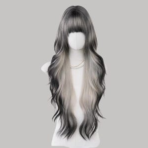 May include: A long, wavy wig with a mix of black, gray, and white tones. The wig features a full fringe and is styled on a mannequin head. The hair cascades down the shoulders in loose waves, creating a layered effect.