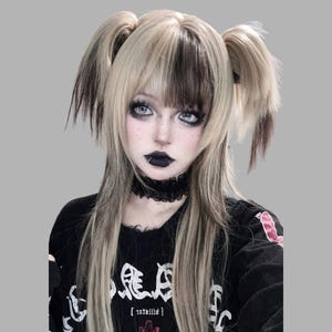 May include: A person with a two-toned blonde wig with dark streaks, styled in pigtails and bangs. They wear a black choker and a black long-sleeved shirt with white text. The person has dark eye makeup and black lipstick.