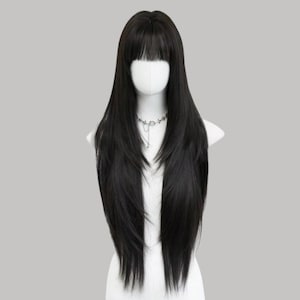 Puede incluir: Una peluca larga y negra con flequillo recto, peinada sobre un maniquí. La peluca presenta mechones en capas y una línea de cabello de aspecto natural. Un collar plateado es visible alrededor del cuello del maniquí. El fondo es gris neutro.
