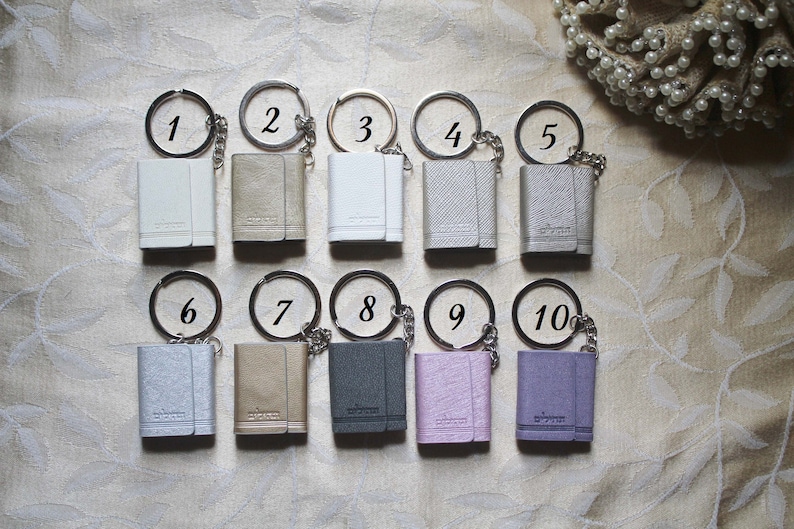 May include: Ten small, rectangular keychains with different coloured leather covers and silver key rings. The keychains are numbered 1 through 10.