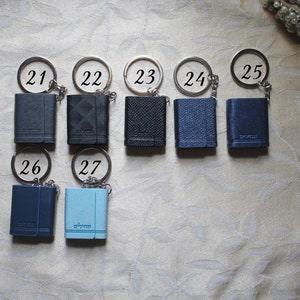 May include: A set of ten small, leather-bound notebooks with keychains. The notebooks are numbered 21 through 27 and are in shades of blue and black.
