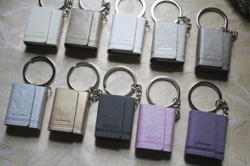 May include: Ten small, leather-bound keyrings with silver key rings. The keyrings are in various colours, including silver, gold, black, white, pink, and purple. Each keyring has the word "sticker" embossed on the front.