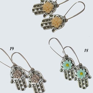 以下が含まれることがあります： 花柄のアクセントが付いた銀色のハmsaハンドイヤリングが3ペア。イヤリングはフック留めです。花は、ピーチ、ライトグリーン、ダークグリーンの3色です。