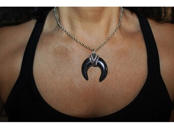 May include: A silver chain necklace with a black crescent moon pendant. The pendant is adorned with small, clear rhinestones.