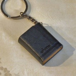 May include: A small black leather book keychain with a silver key ring. The book has the word "edition" embossed on the cover.