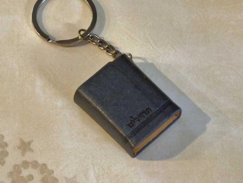 May include: A small black leather book keychain with a silver key ring. The book has the word "edition" embossed on the cover.