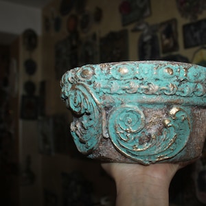 May include: A turquoise and gold planter with ornate detailing. The planter is made of a textured material and has a distressed finish.