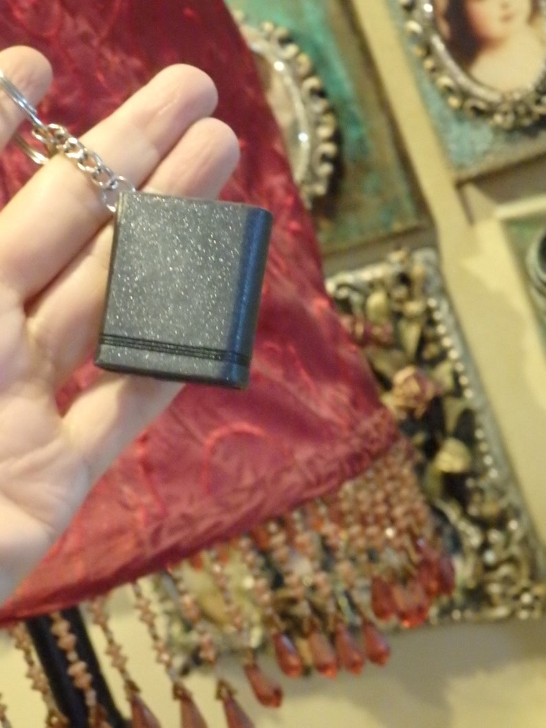 May include: A small, black, sparkly book-shaped keyring with a silver chain.