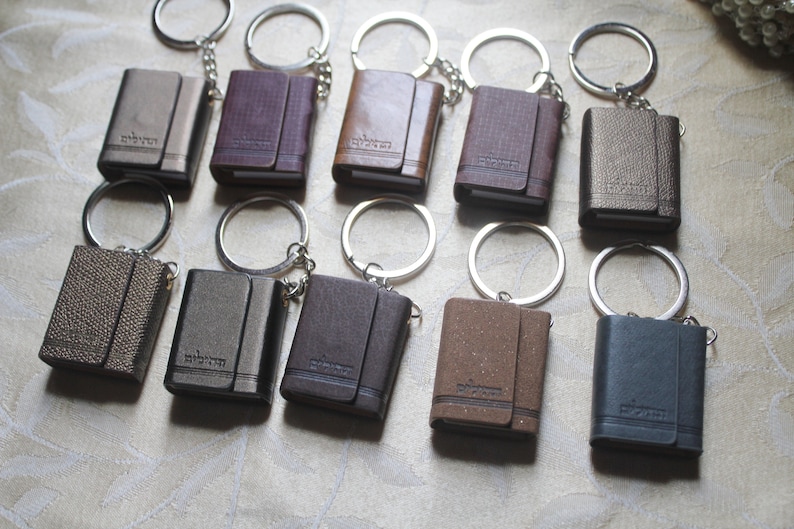 May include: Ten small leather-bound notebooks with keychains. The notebooks are in various colours, including brown, black, grey, and gold. Each notebook has a silver keychain attached to it.