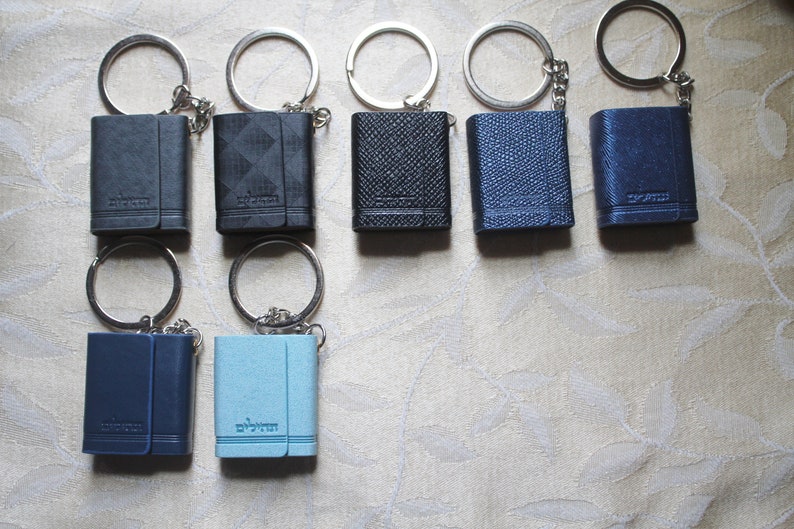 May include: Eight small leather-bound keychains with silver rings and chains. The keychains are in various shades of blue and black.