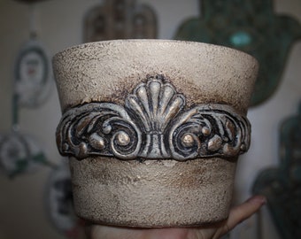 May include: A decorative ceramic planter with a distressed white finish and a gold-coloured embossed design around the top.
