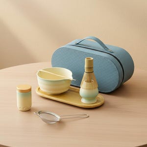 May include: A matcha tea set with a light blue carrying case, a bamboo whisk, a ceramic bowl, a small container, a bamboo tray, and a metal sieve. The bowl and container have a gradient color scheme. The set is arranged on a wooden table.