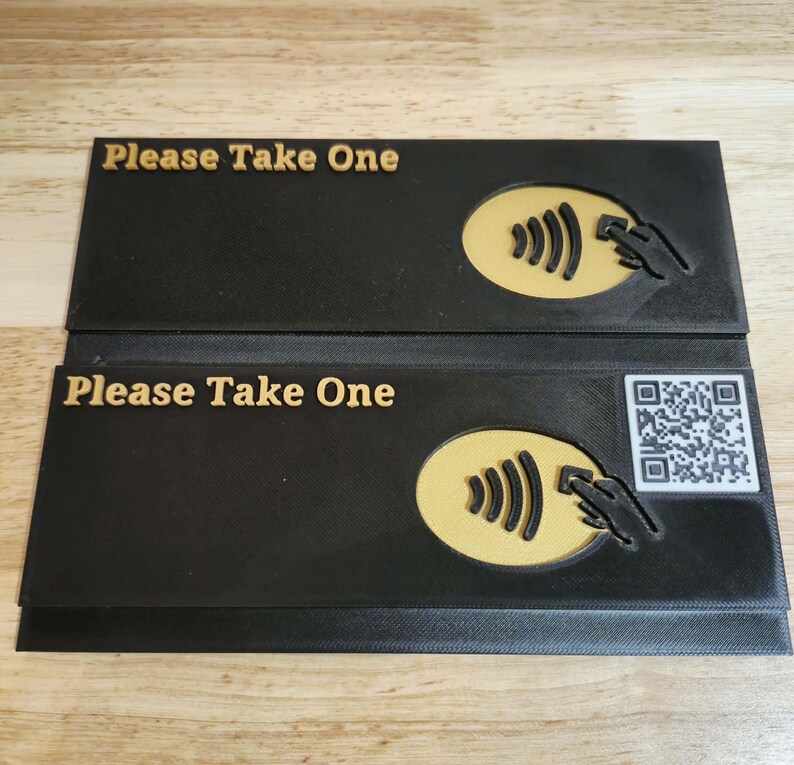May include: Two black rectangular signs with the text "Please Take One" in gold. Each sign features a gold contactless payment symbol and a hand icon. One sign also has a QR code.