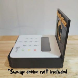 May include: A black and white SumUp card reader case with a stand. The case has a slot for the card reader and a stand with the text "Pay Here" in gold. The SumUp device is not included.