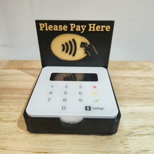 May include: A white and black SumUp card reader with a display and number pad. The reader is in a black stand with the text "PLEASE PAY HERE" and a contactless payment symbol.