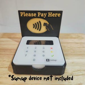 May include: A black and white SumUp card reader stand with the text "Please Pay Here". The stand has a white keypad with numbers and a SumUp logo. The text "Sumup device not included" is at the bottom.
