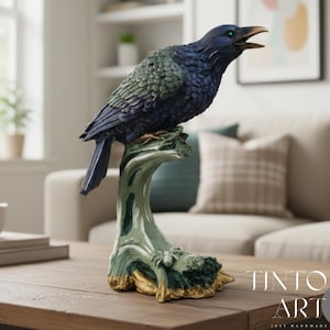 May include: A detailed raven sculpture perched on a stylized tree branch. The bird features a dark blue body with green accents, open beak, and green eyes. The branch is painted in shades of green and gold. The sculpture is displayed on a wooden table.
