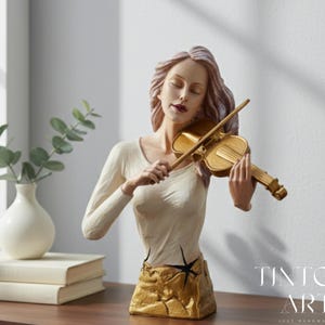 Könnte beinhalten: Dekorative Büste einer Frau, die eine goldene Geige spielt. Die Skulptur hat ein cremefarbenes Oberteil und einen strukturierten, goldfarbenen Sockel. Die Frau hat lange, wellige Haare und ist mit geschlossenen Augen dargestellt.